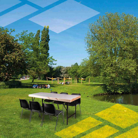 Black plastic stacking chairs set up outdoors near a table by a pond.